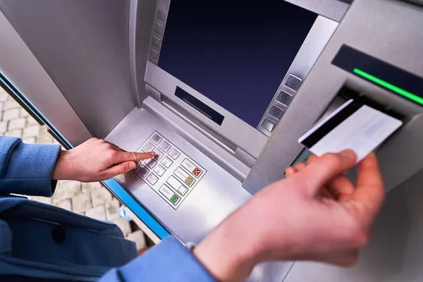Osoba korzysta z bankomatu: naciska przyciski klawiatury i trzyma kartę przy czytniku.